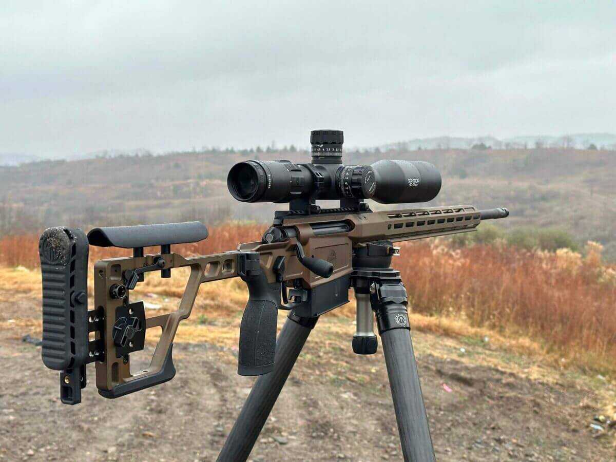 A rifle sits on a tripod on a misty, cloudy day with the Sightron SVIII mounted on it