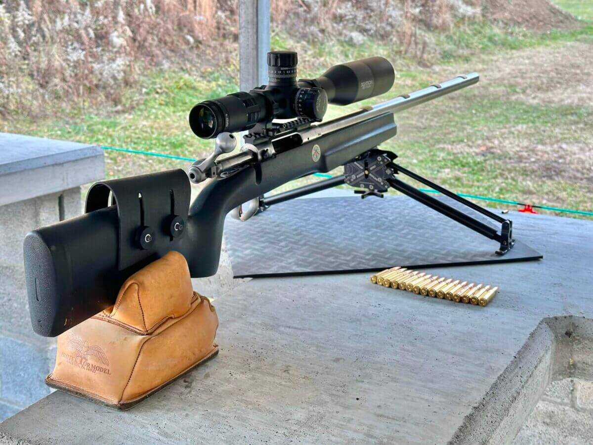 A rifle sits on a bench at the gun range, ammo layed out beside it.