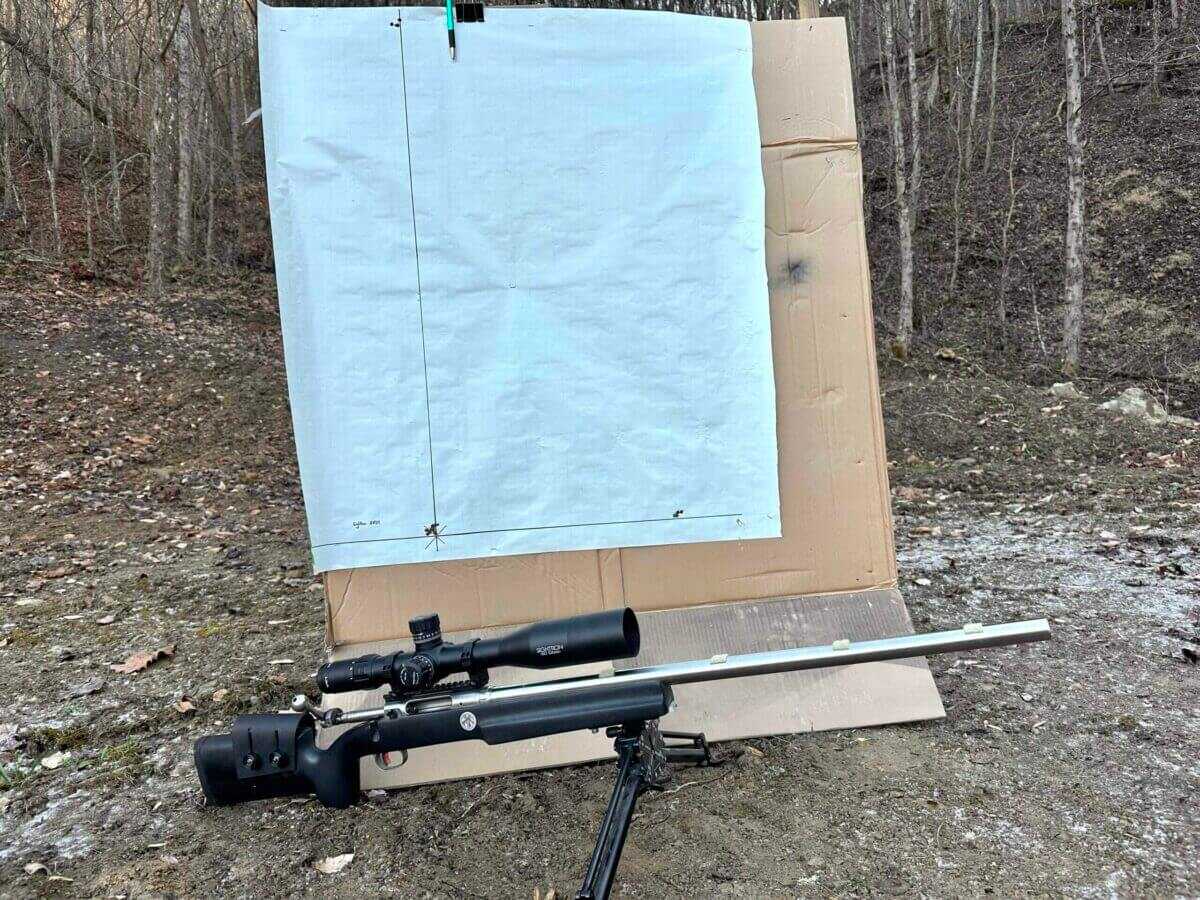 A rifle mounted with the Sightron SVIII lays in front of a tall target that was used for a turret tracking test.