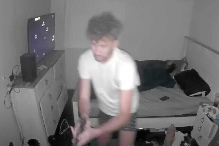 A man standing in his bedroom holding a pistol.