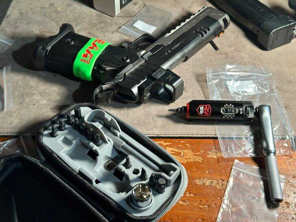 A handgun is getting a red dot installed. The gun and tools rest on a tabletop.