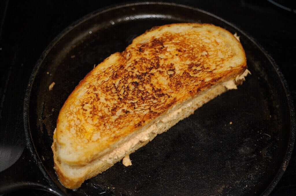 Golden brown grilled fish sandwich toasting on the griddle, ready to flip.