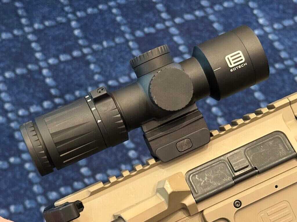 Side view of a black compact scope on a tan AR style rifle.
