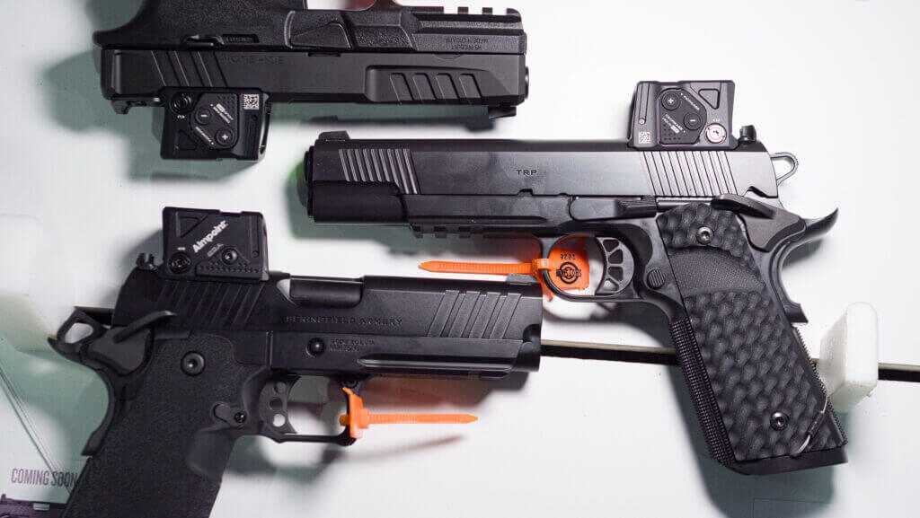 Three guns grouped on a table all with optics attached.