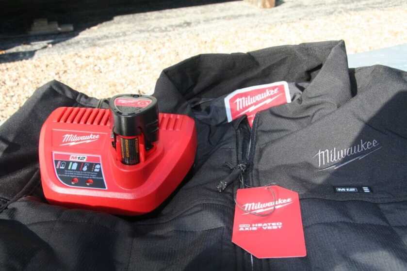 Milwaukee M12 Axis heated vest with battery and charger laid out on bench