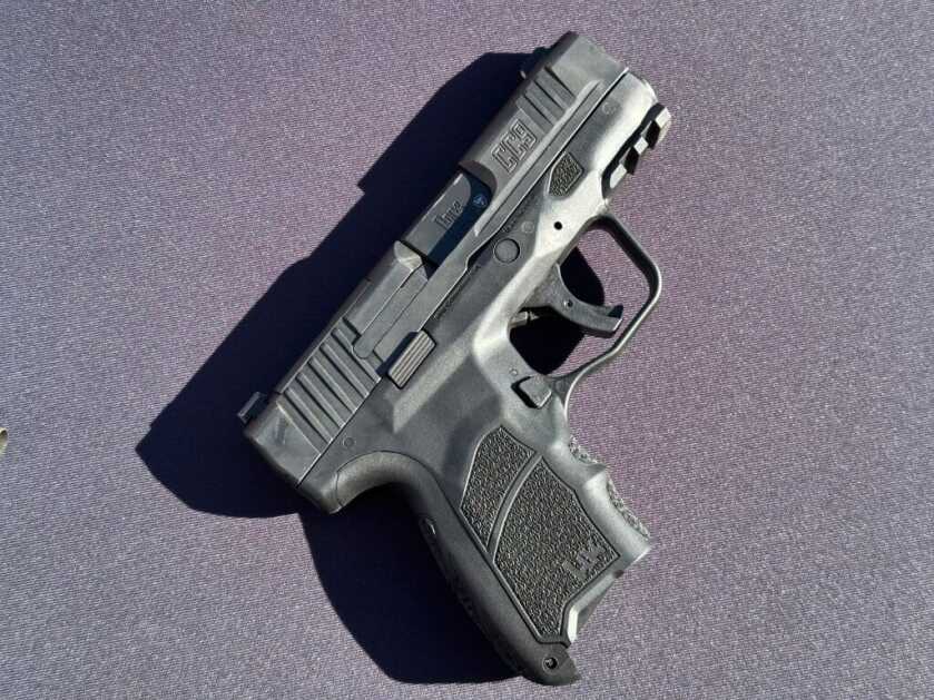 A black handgun lays on a black background, pointing up to the right.