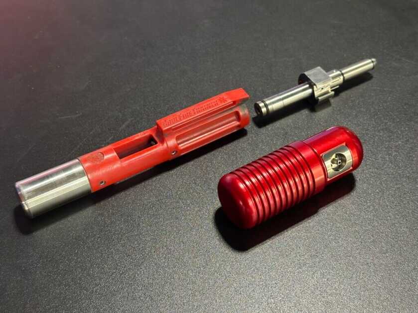 Closeup of a disassembled training system for the AR15. The parts are red, laying on a black table.