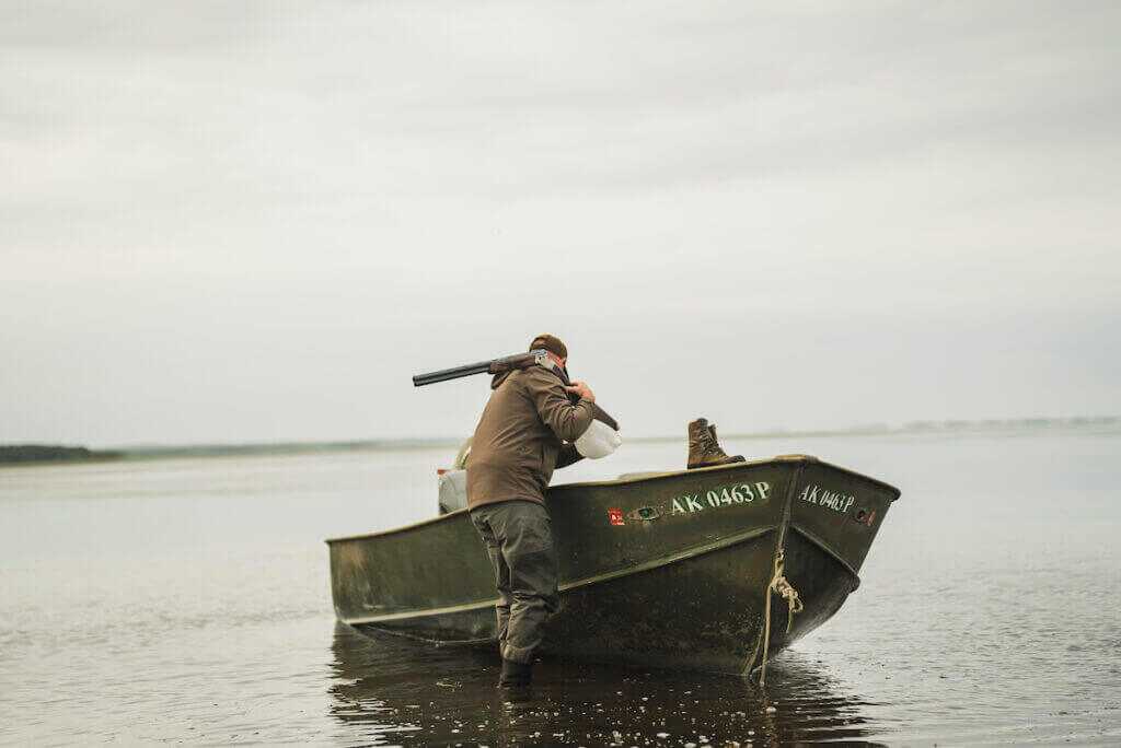 Hunter waiding through water to his boat with a shotgun over his shoulder