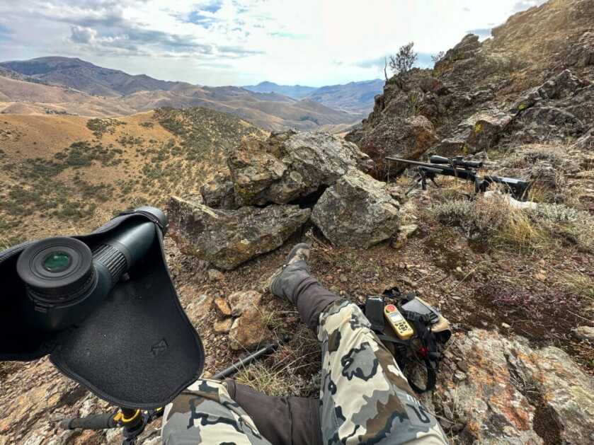 Fireside Stories: How I Killed My Smallest Bull Elk on The Best Tag I've Ever Had - Part 1 of 3 A hunter sits on top of a rocky outcropping, with his gun and spotting scope set up for a shot.