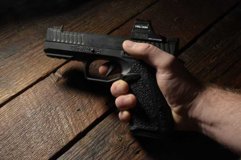 A hand model holds a handgun for a closeup in moody lighting and a wooden table top background.