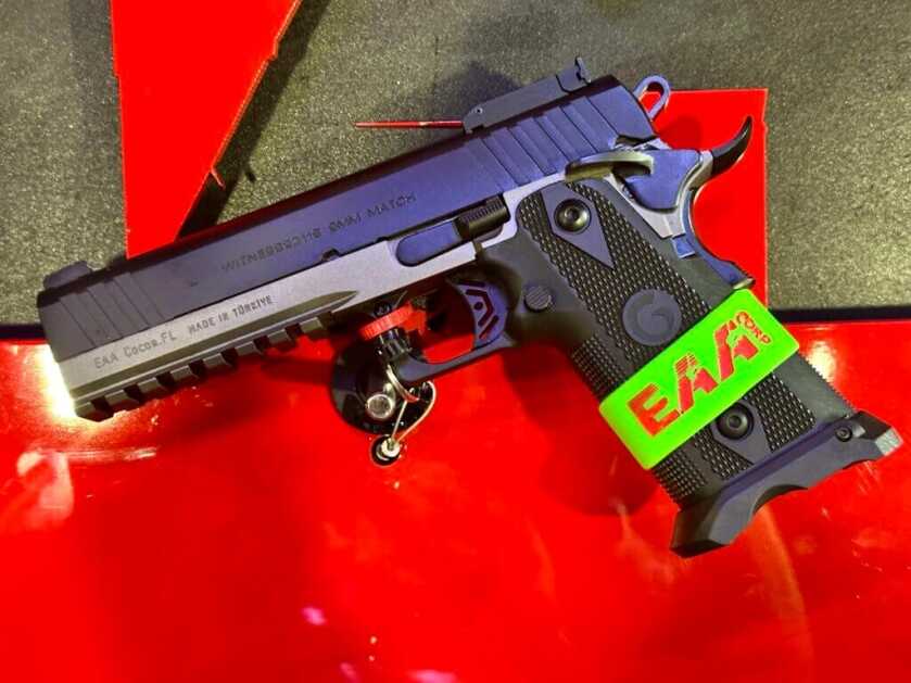 A black handgun lays on a red background. It is laying on it's side and pointing to the left.