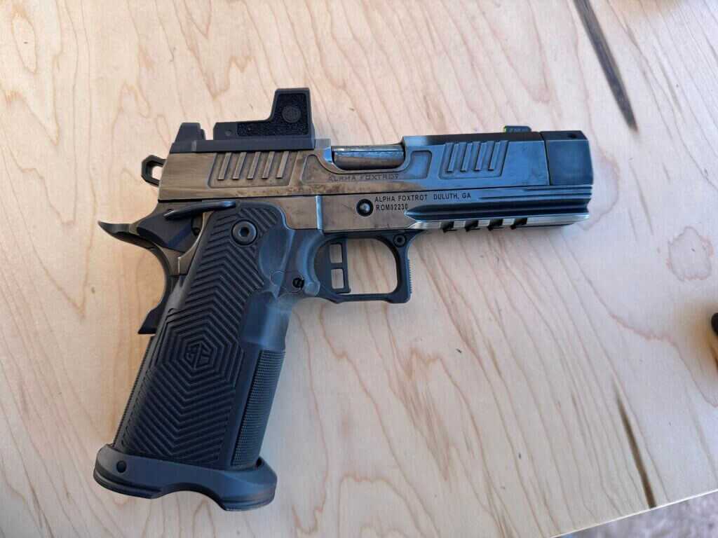 A highly polished black handgun sits on a wooden table, pointing to the right.