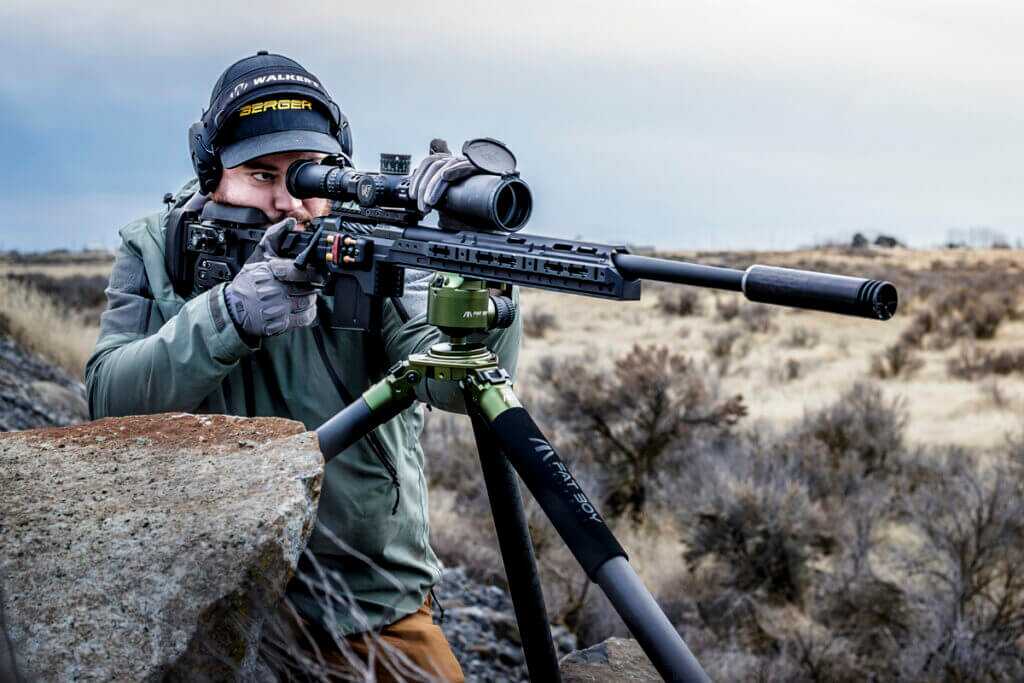 Man in warm clothes looking through scope mounted to KRG rifle out in dry brush