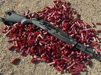 A black shotgun lays on a pile of red shotgun shells on the ground.