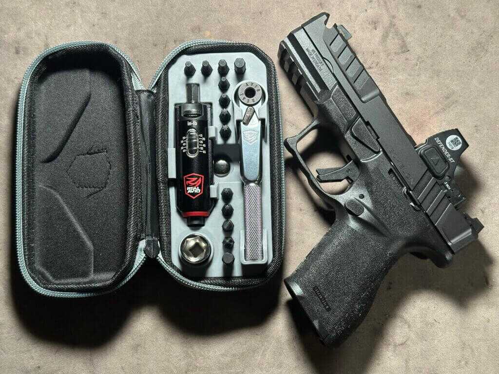 A handgun with an optic is next to a tool kit.