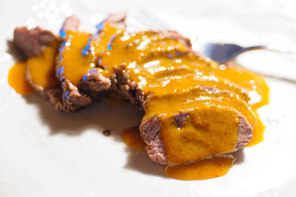 golden currant sauce poured over thinly sliced steak medallions on a white plate.