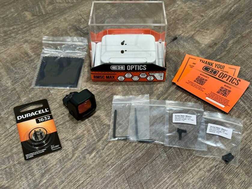 A red dot and the included contents of its packaging are laid out on a wooden backdrop. 