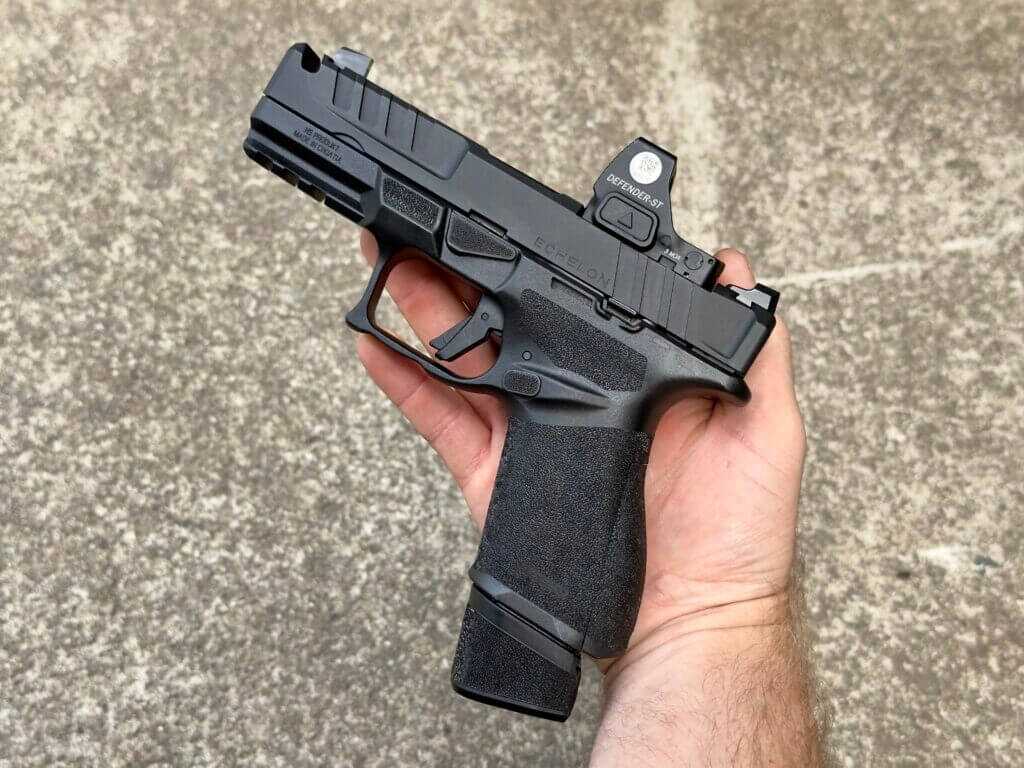 A black handgun rests in a man's hand against a concrete background.