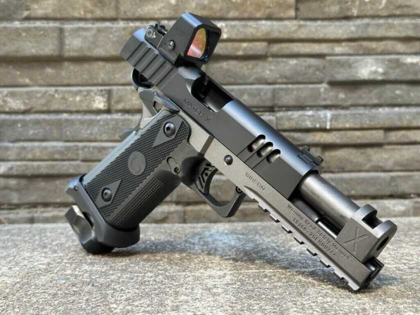 A black and silver handgun is posed in front of a rock wall and concrete floor.