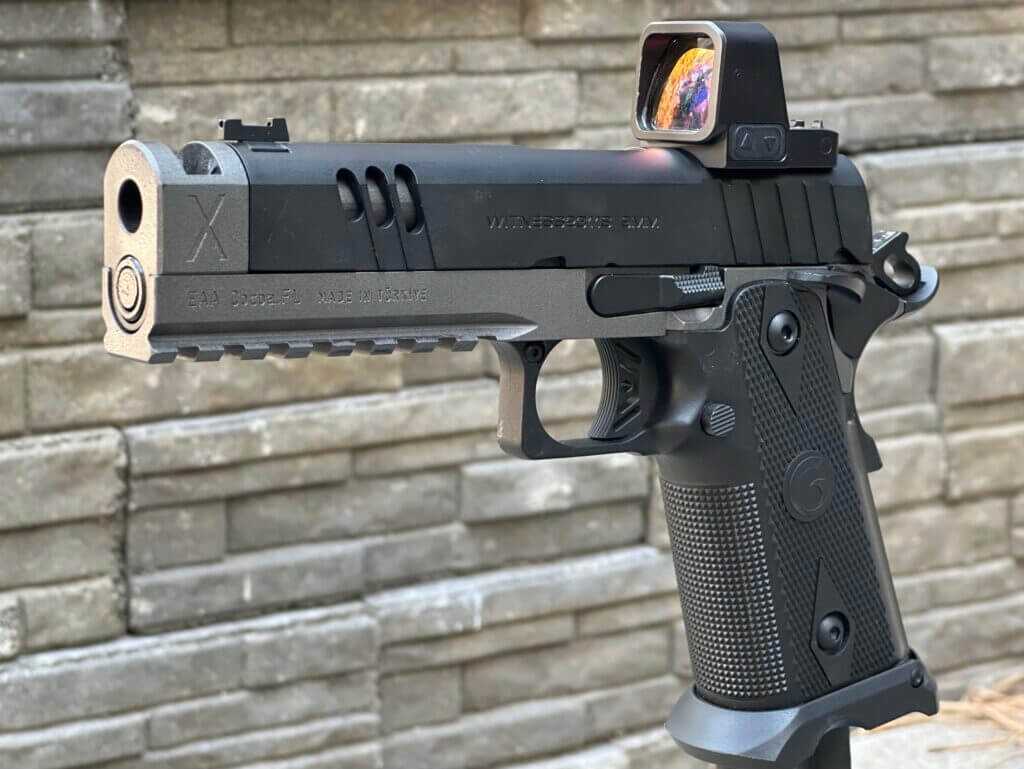 A handgun with red dot optic is posed in front of a stone backdrop. MAX