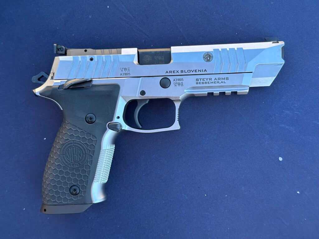 A silver gun sits on top of a blue table. It has black accents.