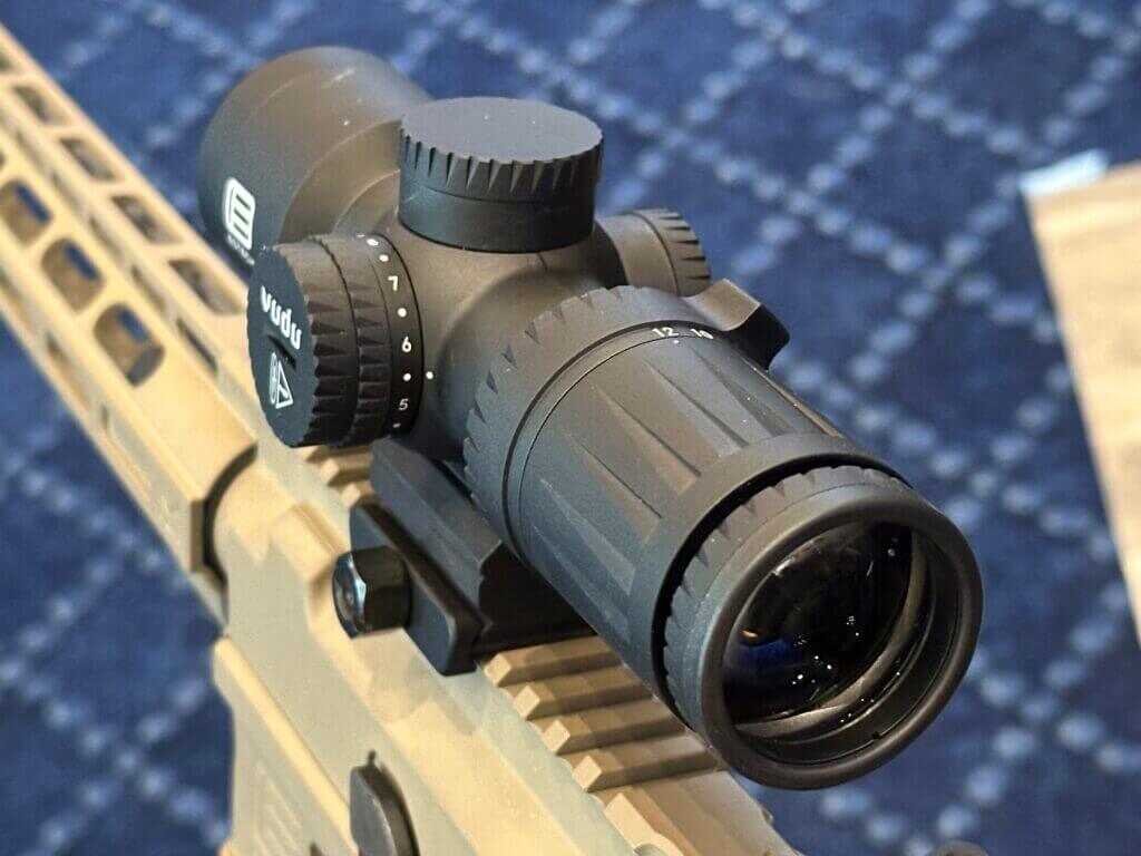 View of the riflescope from the left, rear side looking down. This is a black rifle scope mounted on a tan AR style rifle.