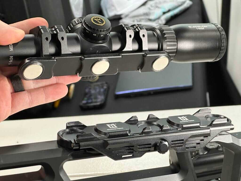 The optic is being removed from the magnetic base. You can see both the ring mount and the magnetic base's interlocking geometry.