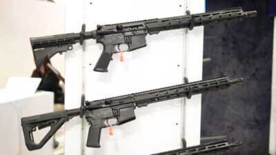 two AR-15s hanging on a white wall rack pointing right.