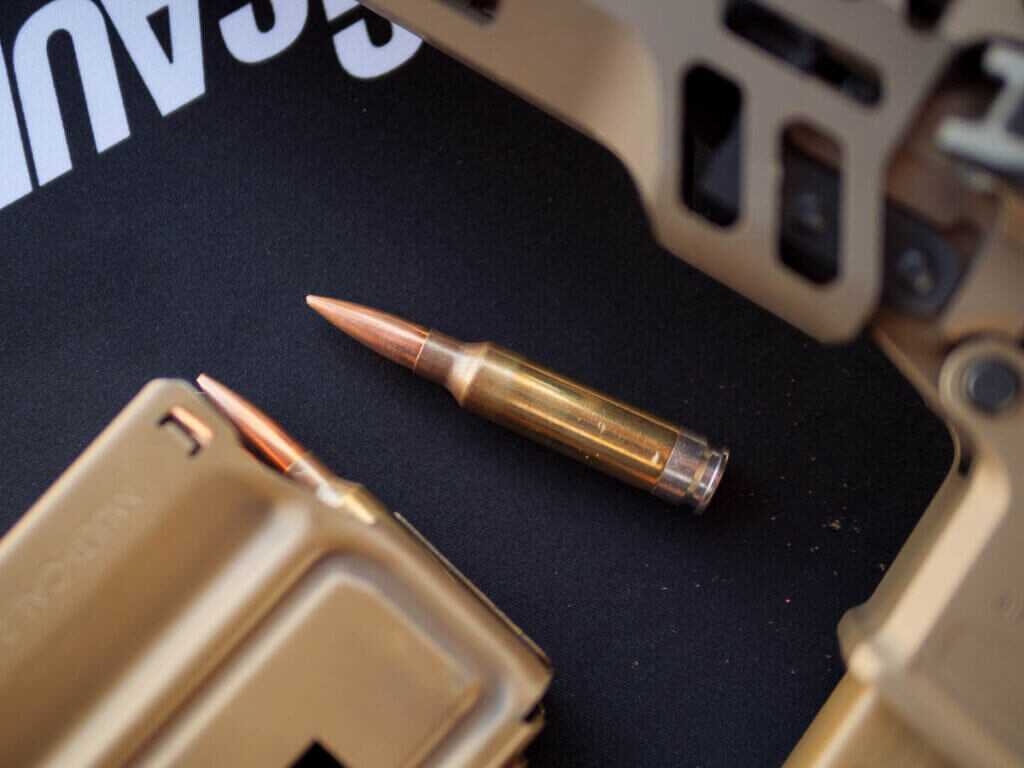 closeup of the cartridge on a black matt with the rifle and a loaded magazine next to it.