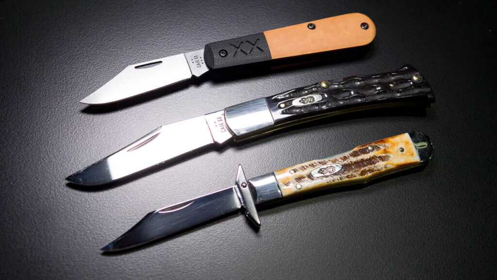 All three knives lying on a black table, blades open, tips to the left.
