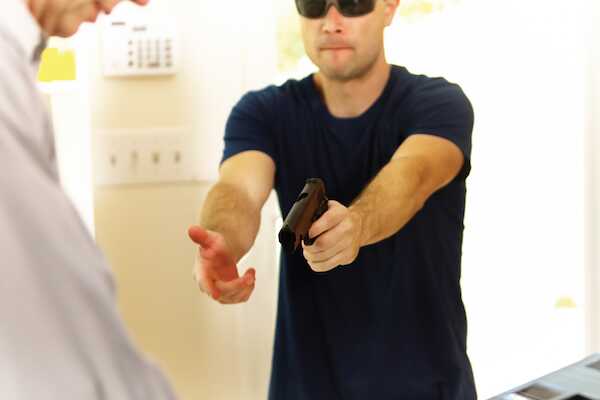 A robber enters a store and demands money from the cash register while pointing a gun at the store employee.