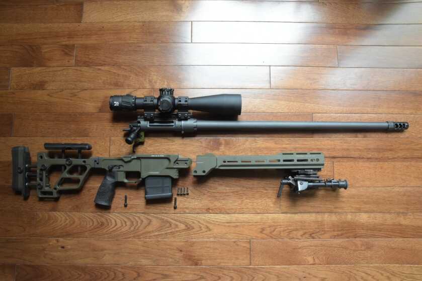 A rifle is disassembled in a blown-apart fashion, laying on a red oak hardwood floor.