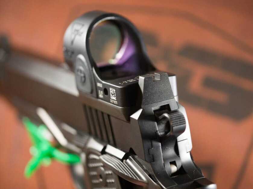 Close up of the back of the gun showing the rear sights and the hammer. There is a red dot optic mounted to the slide. The gun is pointing away and to the left.