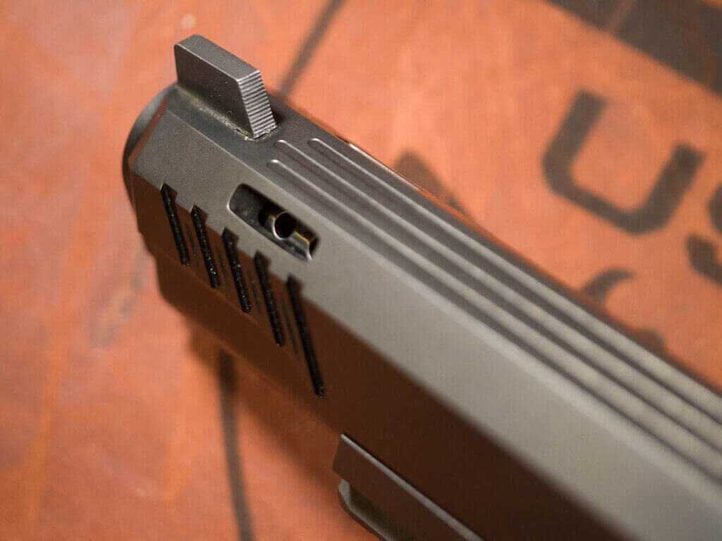 Close up view of the front of the slide including the front sight. The Insurrection's slide is machined with three flat sides and three longitudinal serrations running its length. the gun is pointed away and to the left.