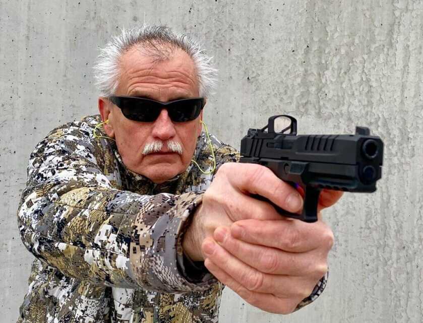 Man aiming pistol with the RMSc red dot in front of cement wall