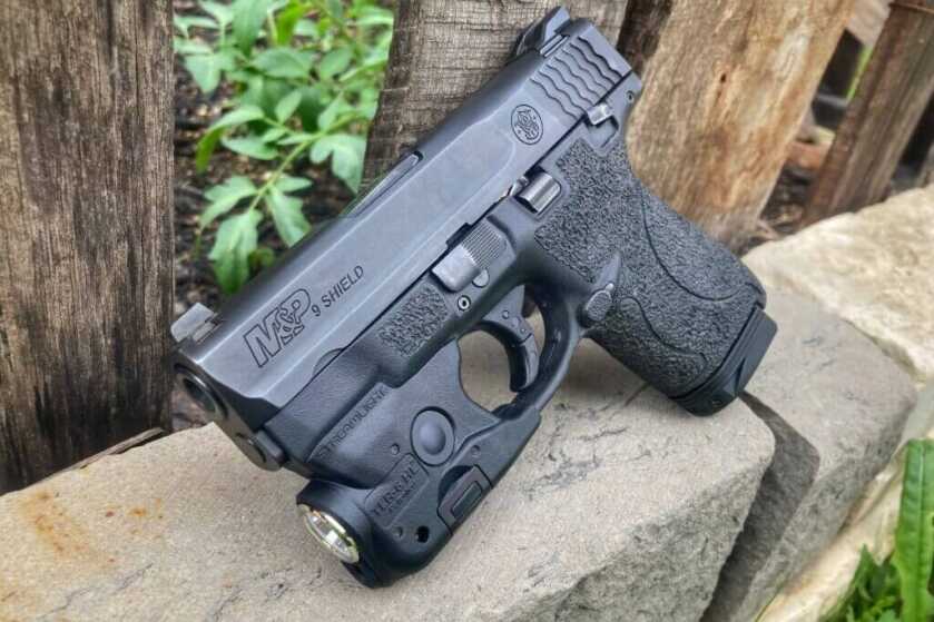 S&W Shield on rock in front of wooden fence