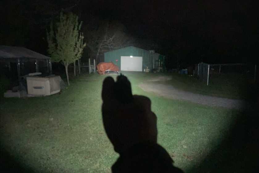 A pistol-mounted light points at a shed