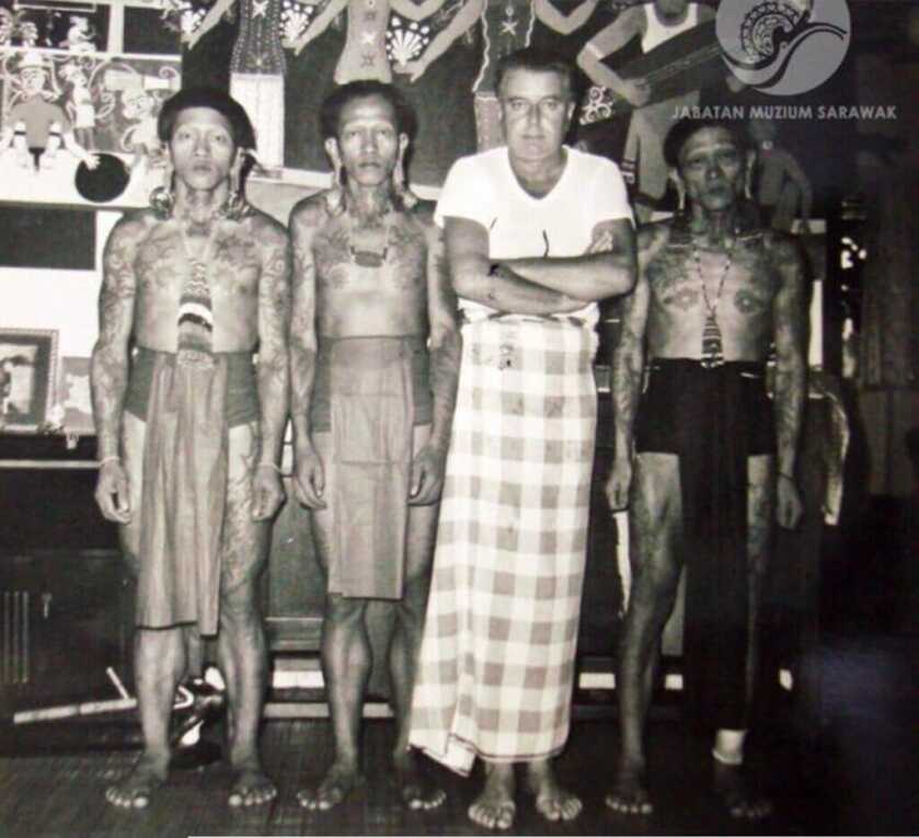 Tom Harnett Harrisson wrapped in checked blanket surrounded by Japanese indigenous men