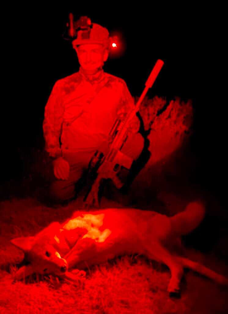 Hunter with coyote, hunting rifle, and thermal gear in red light