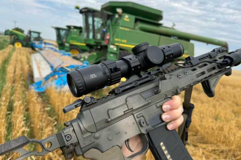 Holding up a rifle with the Arken EP-8 scope mounted in front of a wheat field and a green tractor