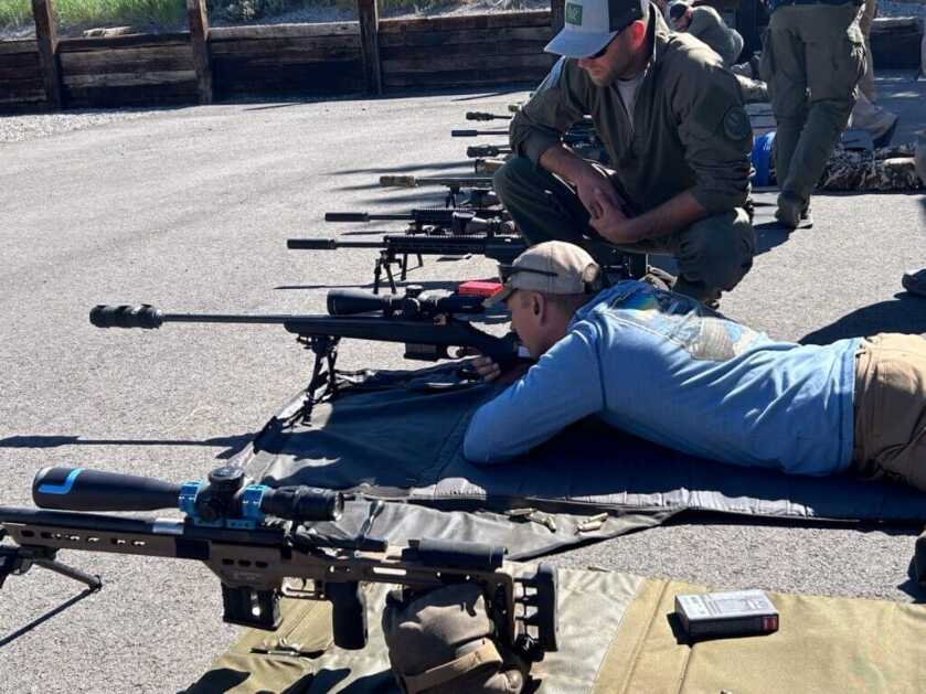 Man lying prone on asphalt looking through a Leupold Mark 4HD scope mounted to a rifle