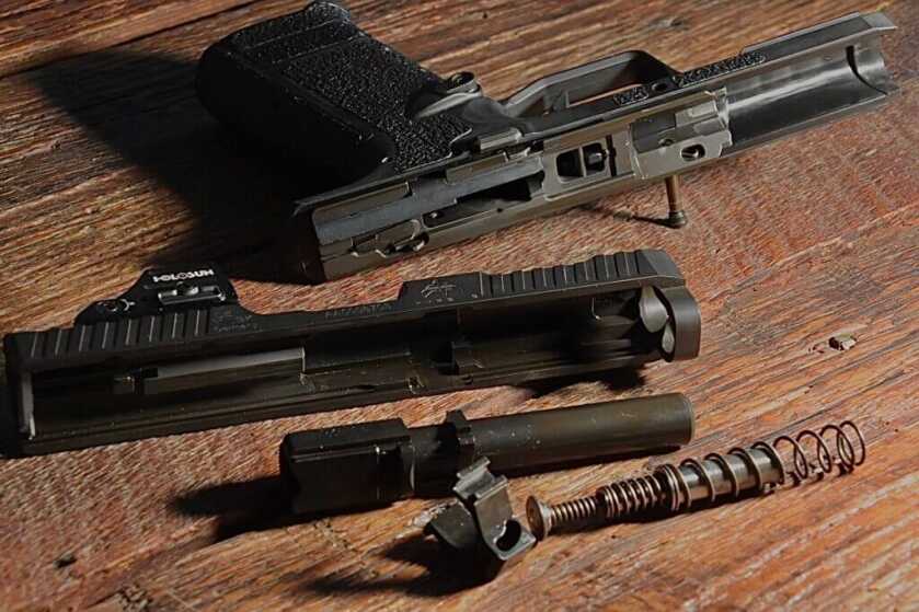 The internals of a handgun are layed out on a wooden table to show their unique design. 