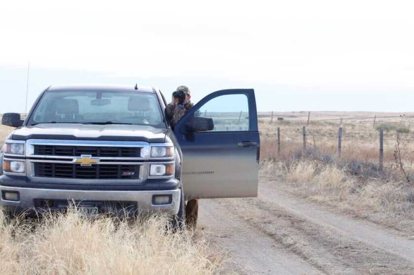 person standing by a truck with binoculars scouting for late season hunting