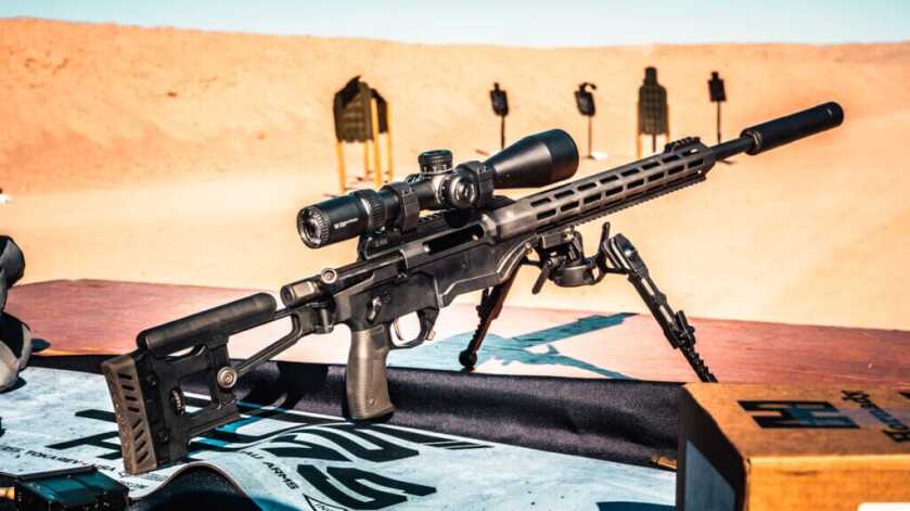 A tactical-style bolt action rifle is perched on the table at the range. 