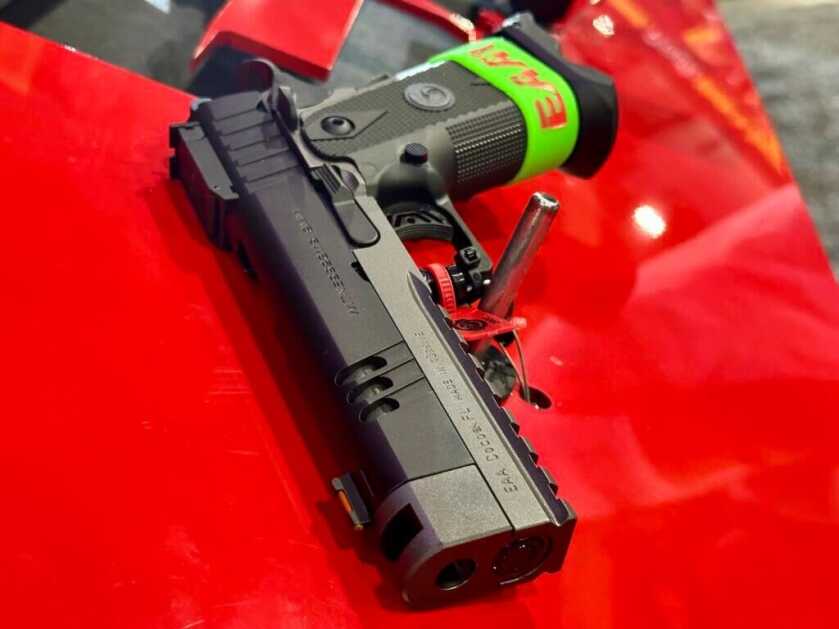 A handgun lays no a red table and points toward us.