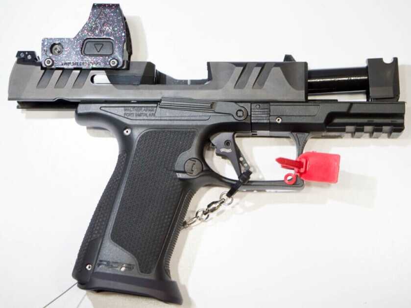 The gun laying on a white table , facing right, with the slide locked open.