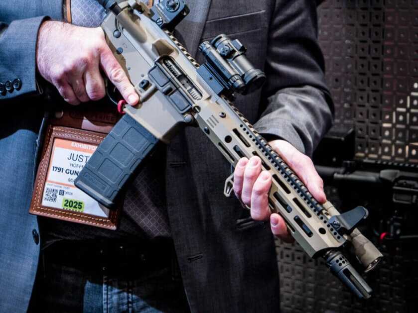 close up of an AR-15 held by a man in a suit. 