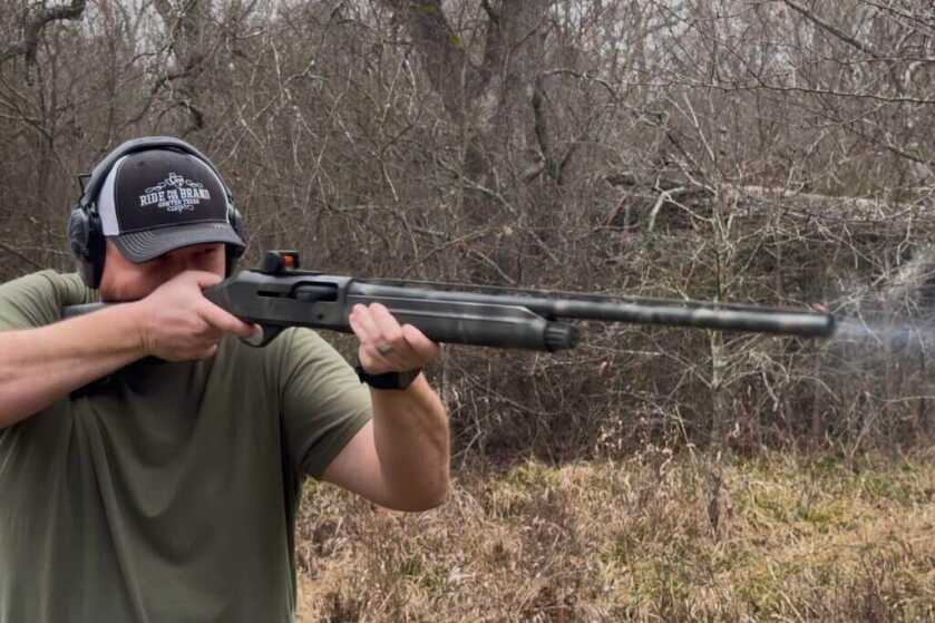 Man shooting a shotgun with a Vortex Viper Red Dot in front of tangly brush