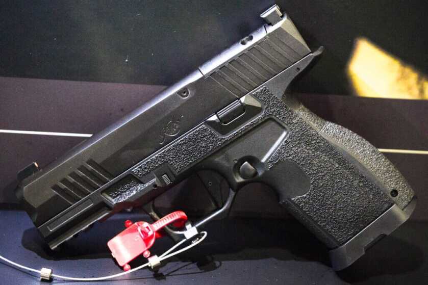 The gun standing on the table with the grip and barrel resting on the table. the left side showing.