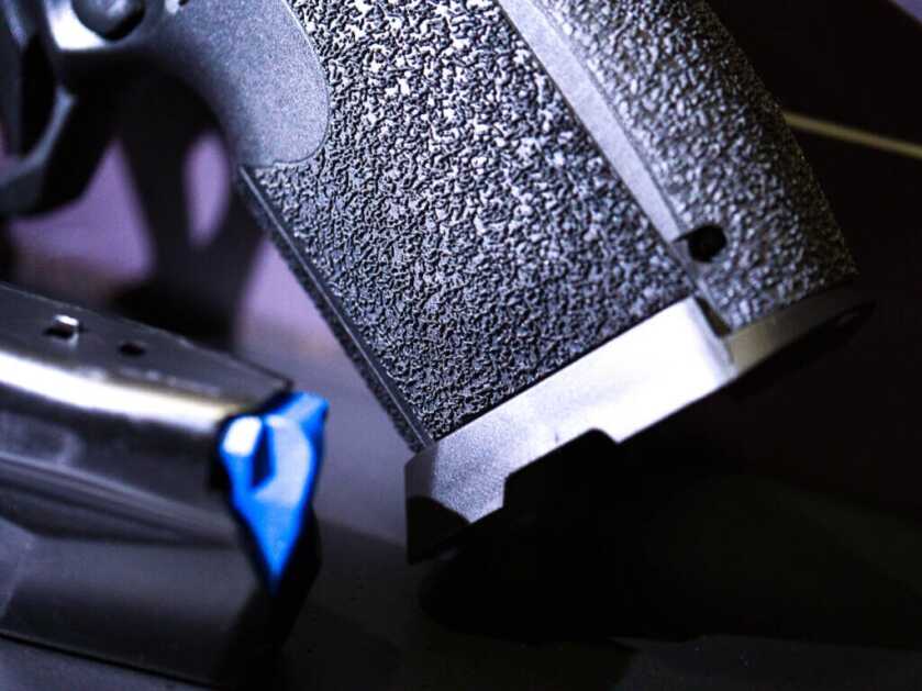 Close up view of the bottom of the grip with the large magwell and a magazine laying next to it.